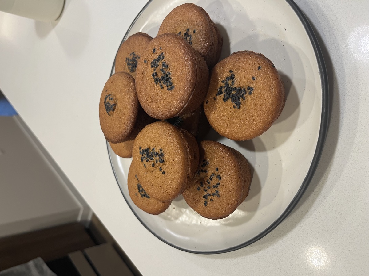 A plate of golden mochi muffins topped with black sesame seeds, on a kitchen counter.