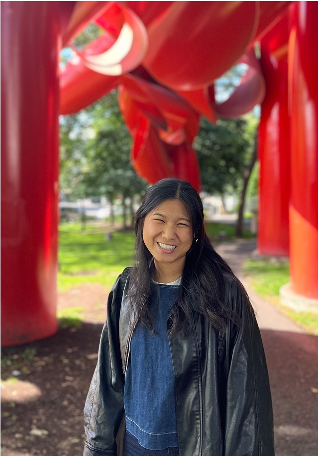 Jasmine smiling in front of a large red sculpture in a park.