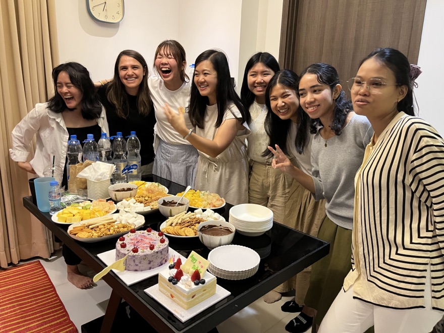 The ISMP Cambodia team and ambassadors laughing together behind a table of cakes and fruit at the farewell.
