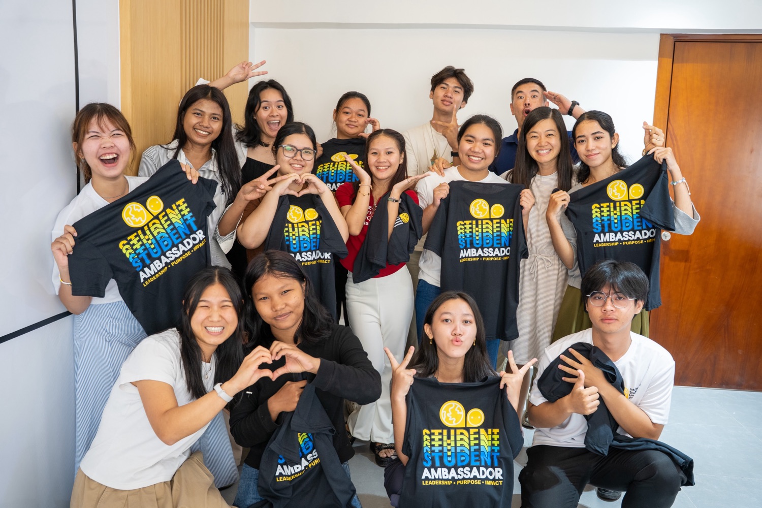 Students holding up Student Ambassador t-shirts, making heart shapes with their hands.