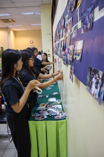 Ambassadors taping printed photos to a purple wall display, building a month-by-month timeline of the year.